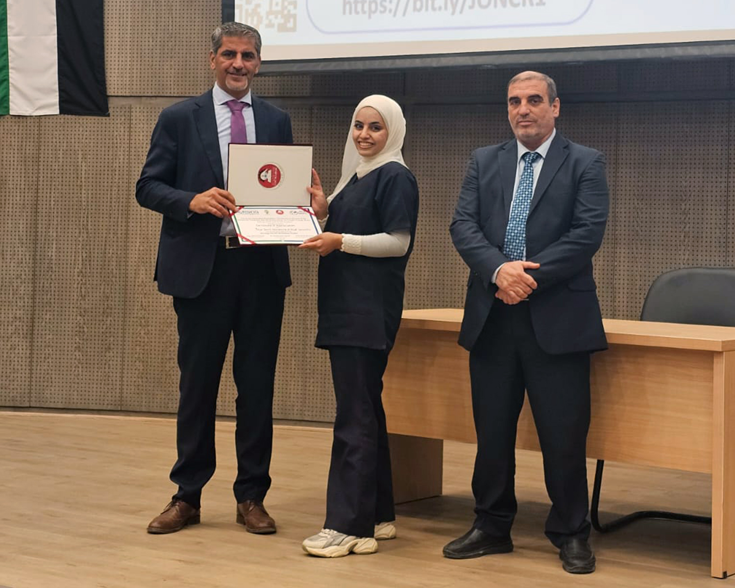 Nurse holding certificate at awards celebration surround by two people